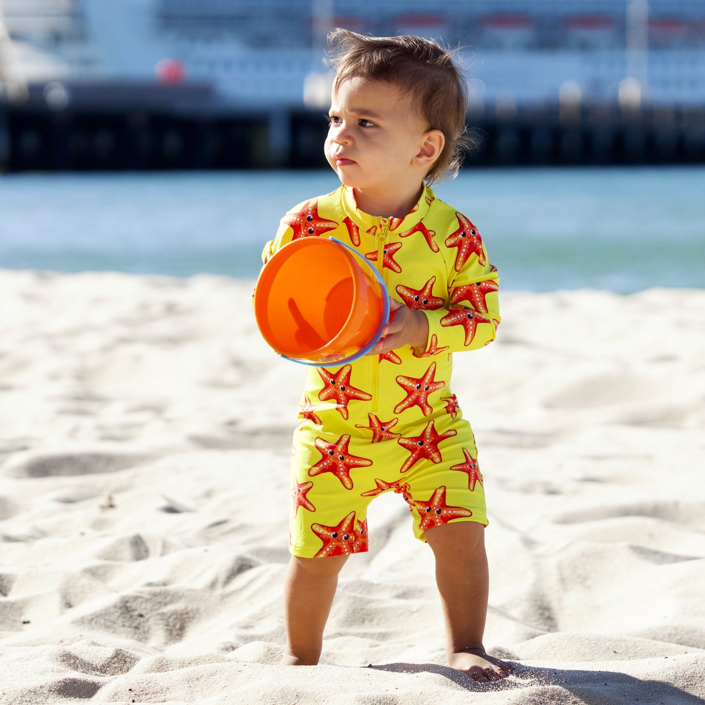 Splashy Tots Yellow baby boy/girl swimwear - Unisex one piece starfish swimsuit - Front view standing at beach