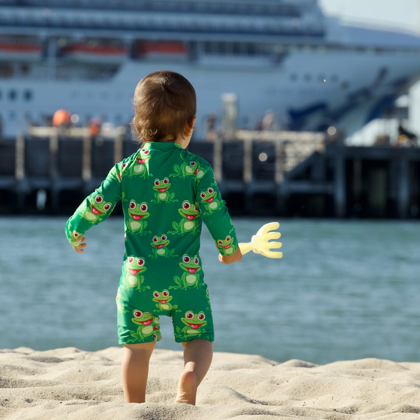 Splashy Tots Green baby boy/girl swimwear - Unisex one piece frog swimsuit - Rear view standing  at beach