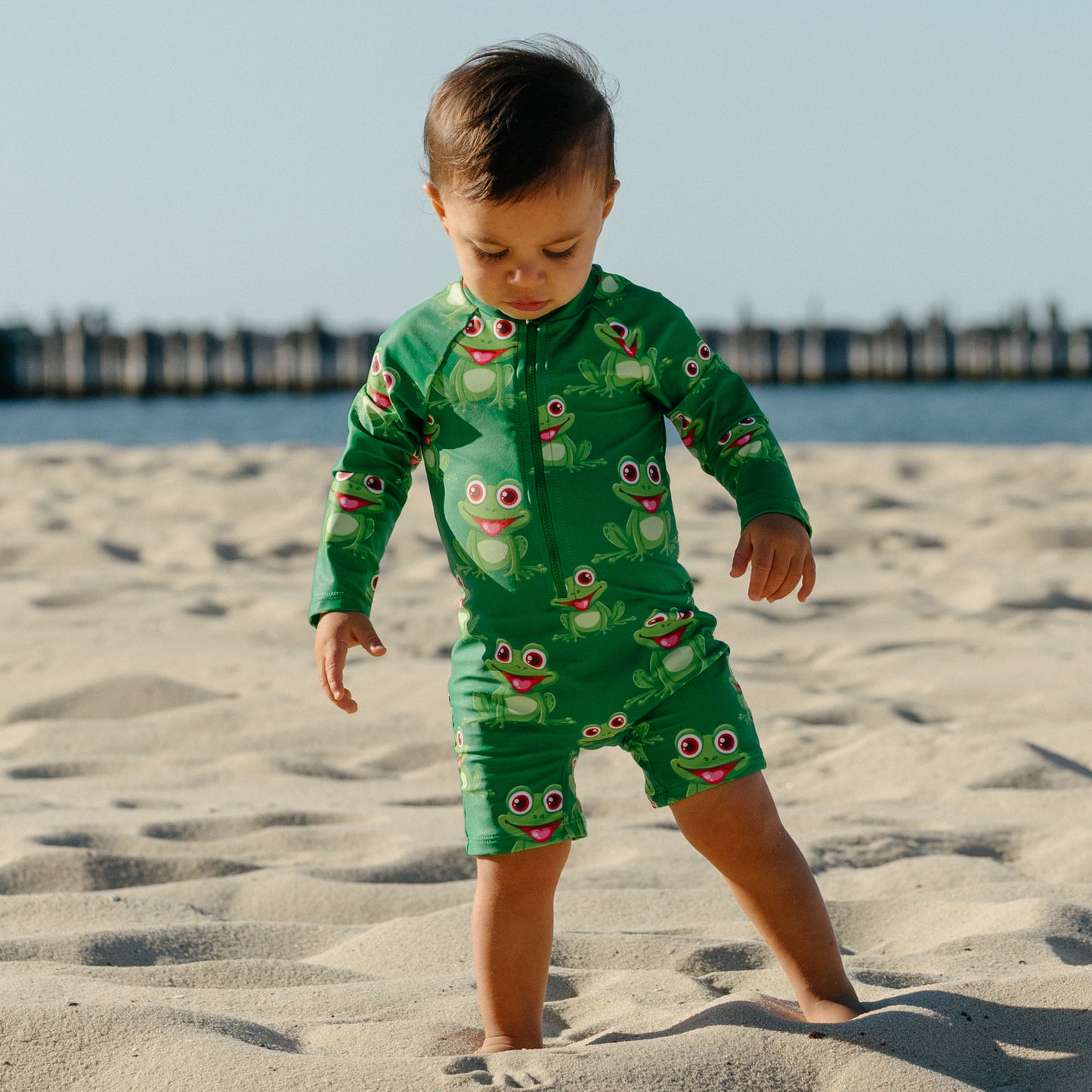 Splashy Tots Green baby boy/girl swimwear - Unisex one piece frog swimsuit - Front view standing at beach